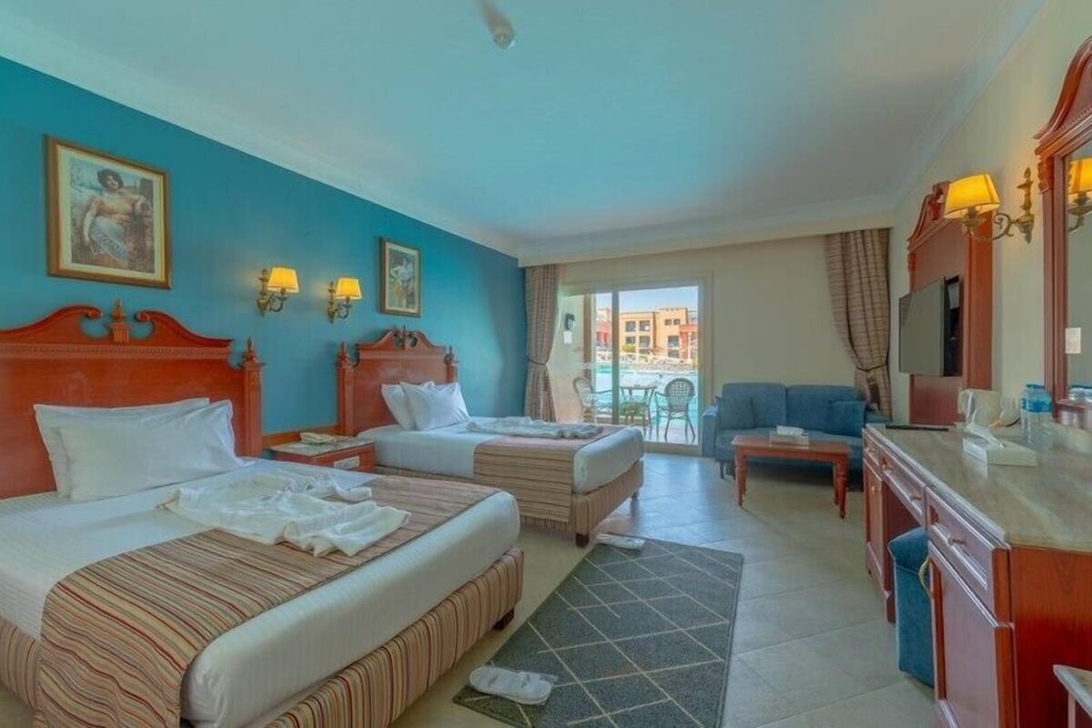 Een hotelkamer met twee bedden, een slaapbank, een televisie en een eethoek.