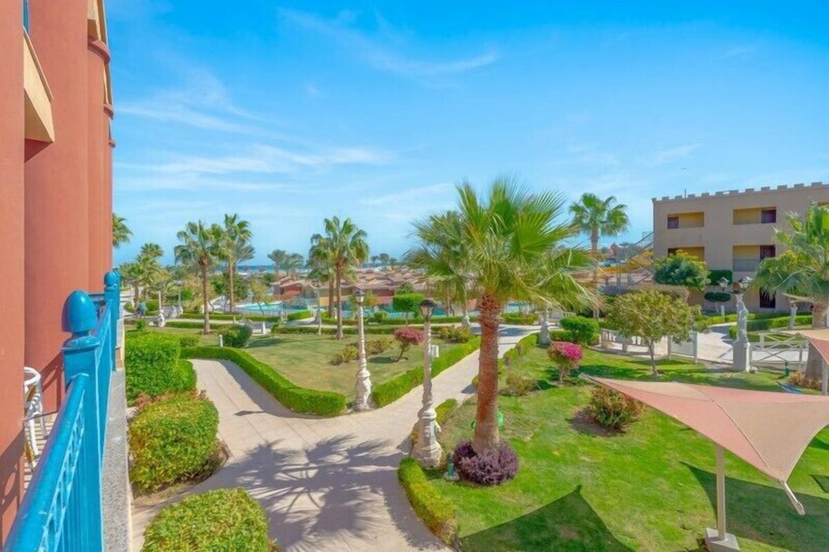 Een hotel binnenplaats met palmbomen, een pad en een gebouw met een blauwe balustrade.