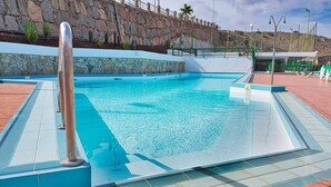 A swimming pool with clear water, a stone wall, and a tiled deck area. - Apartamentos Malibu (Mogan)