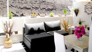 A balcony with a black sofa, a small table, and potted plants. - Apartamentos Malibu (Mogan)