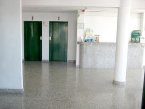 Un vestíbulo con dos ascensores verdes, una recepción con folletos y un piso de granito.