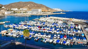 A marina with numerous boats docked, a pier, and buildings in the background. - Apartamentos Malibu (Mogan)