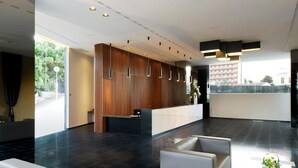 A modern lobby with a reception desk, seating area, and large windows.
