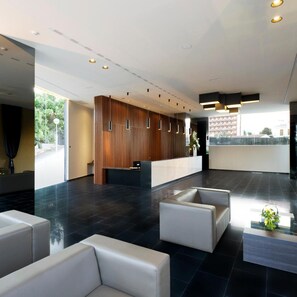 A modern lobby with a reception desk, seating area, and large windows.