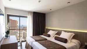 A hotel room with two beds, a desk, and a view of the city.