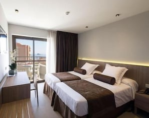 A hotel room with two beds, a desk, and a view of the city.