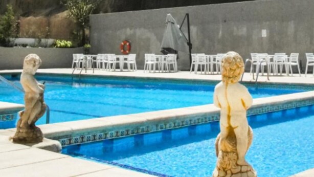 A swimming pool with two stone statues, a lifebuoy, and white lounge chairs.