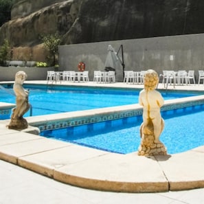 A swimming pool with two stone statues, a lifebuoy, and white lounge chairs.