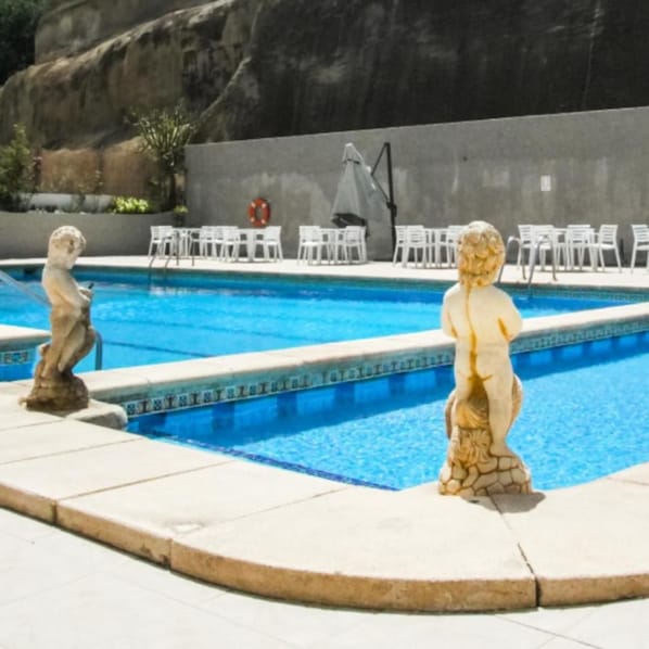 A swimming pool with two stone statues, a lifebuoy, and white lounge chairs.