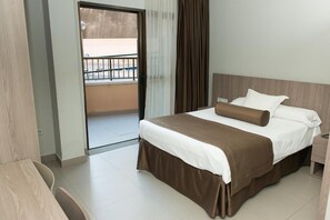A hotel room with a bed, a desk, and a view of the outside balcony.