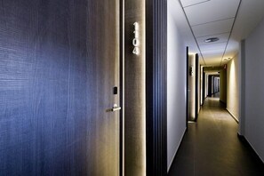 A hotel corridor with a closed door, a number plaque, and a long hallway with doors.