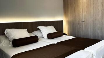 Un lit double avec une tête de lit en bois, une literie blanche et deux coussins décoratifs marron.