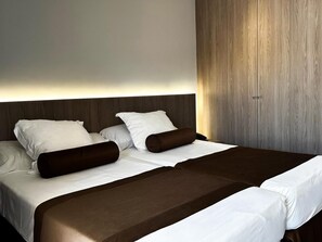 A double bed with a wooden headboard, white bedding, and two brown accent pillows.