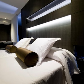 Quarto de hotel moderno com cama bem arrumada, mesa de cabeceira e luminária fixada na parede.