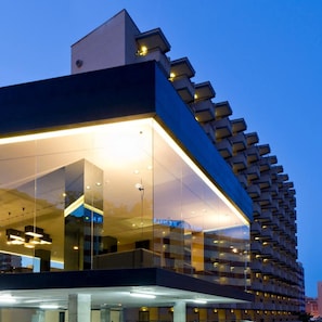 A modern hotel with a glass facade, multiple balconies, and a structured, geometric design.