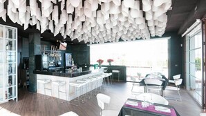 Un espace bar moderne avec un plafond haut, des vitrines contenant des bouteilles et un comptoir avec des tabourets.