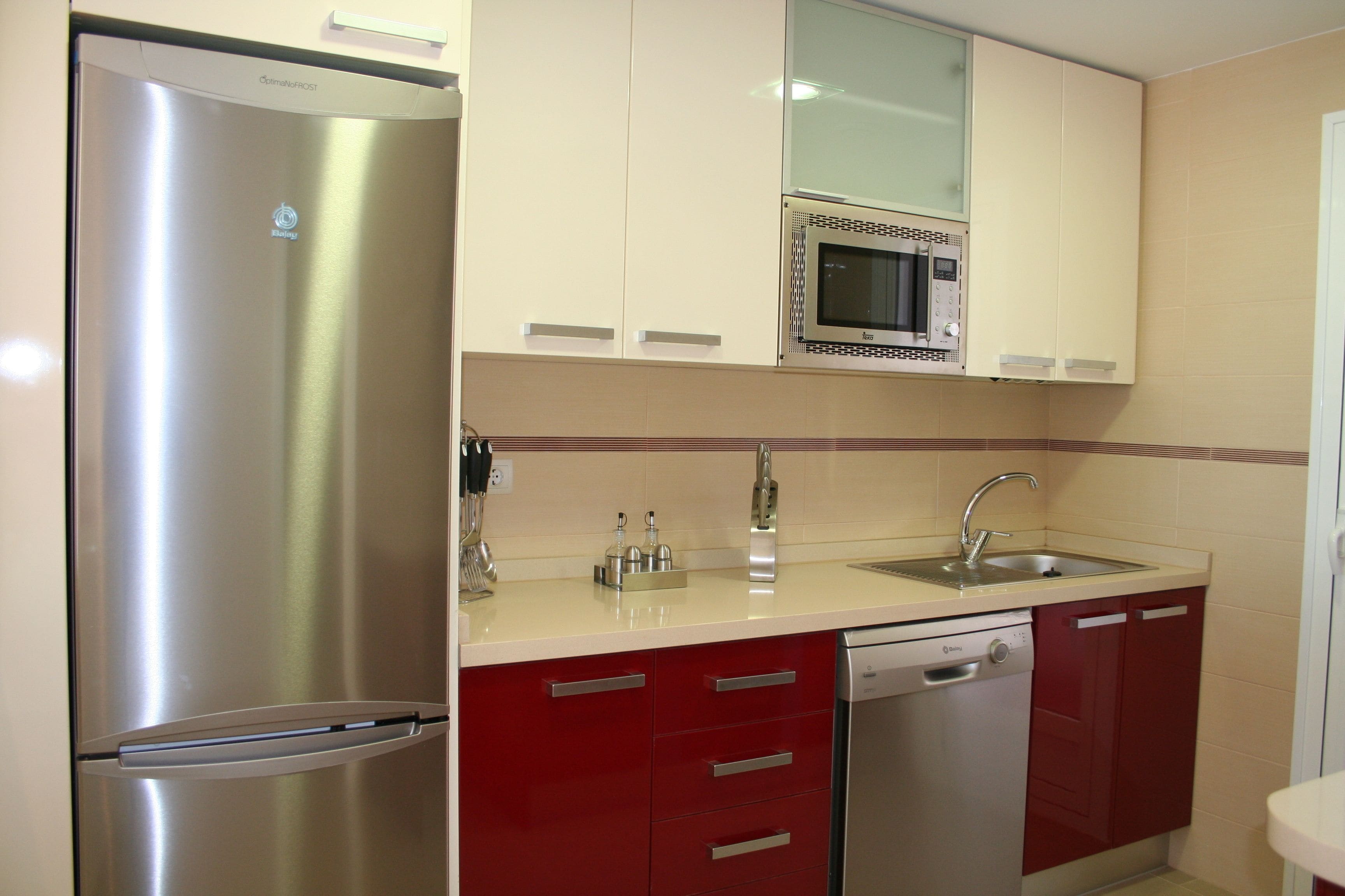 A kitchen with a stainless steel refrigerator, a microwave, a sink, and red cabinets.