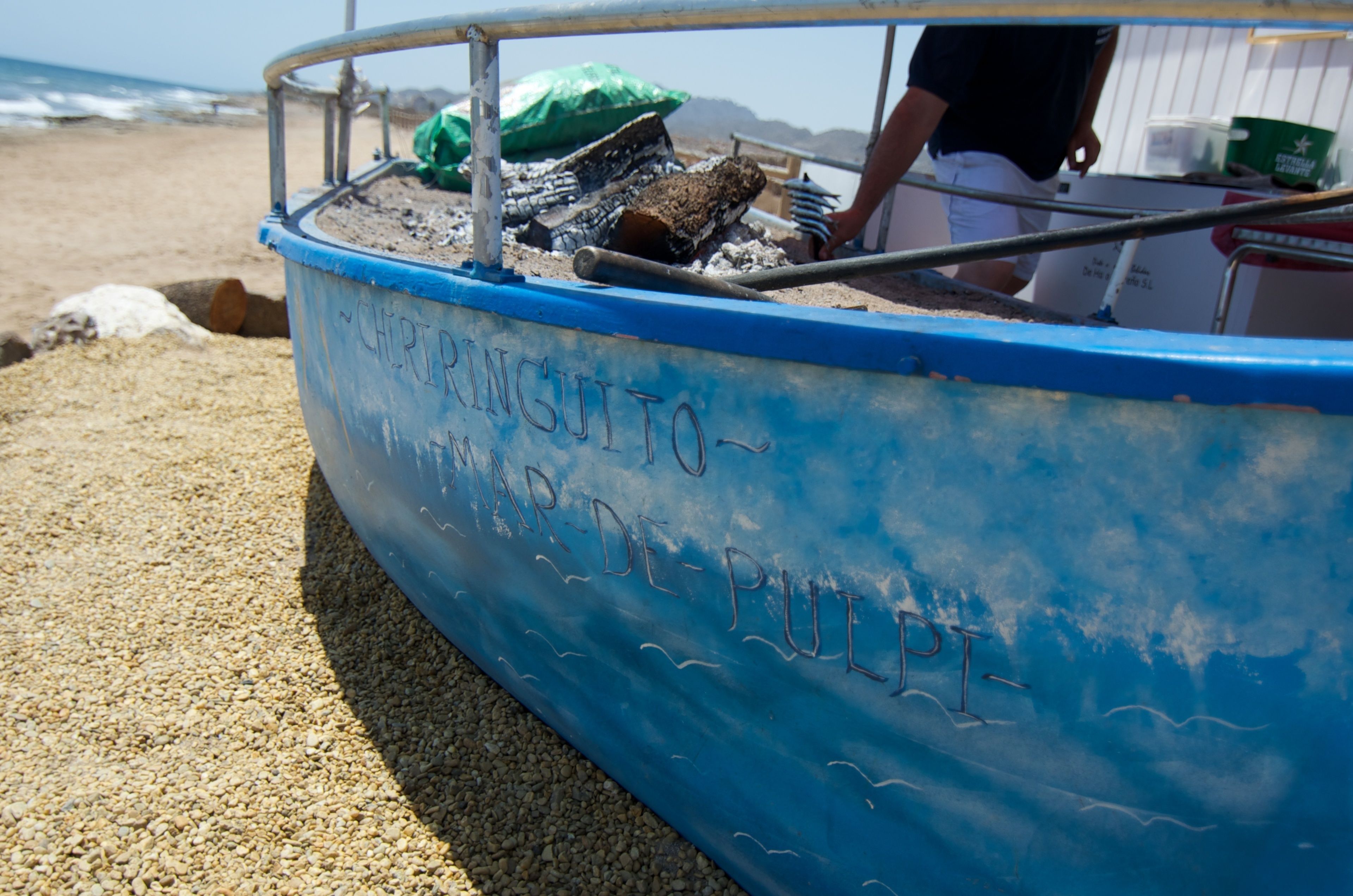 A blue boat with "CHIRIPANGUITO MAR DE PULPI" written on its side, docked on a pebbled beach.