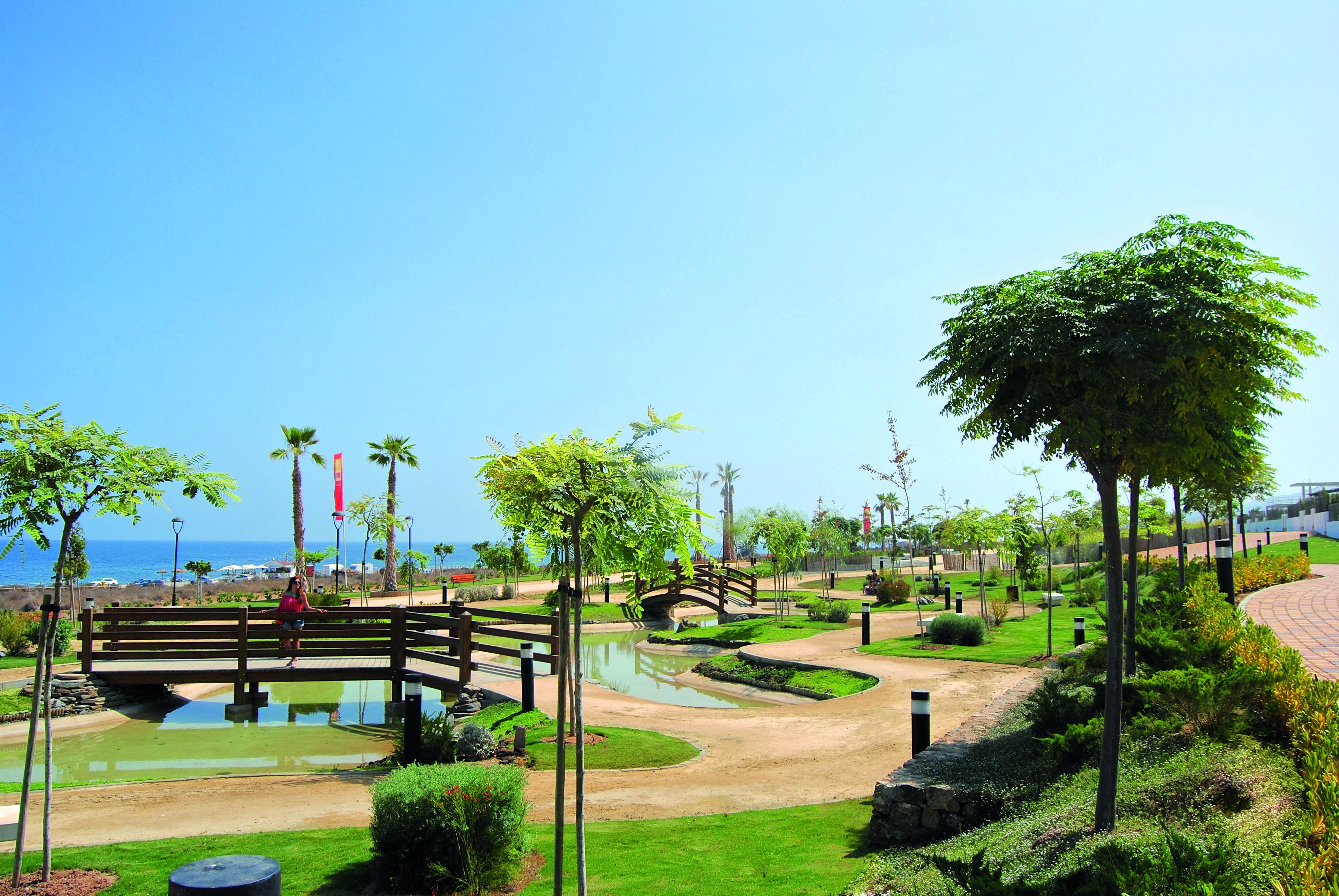 A park with a pond, a wooden bridge, and a view of the sea.