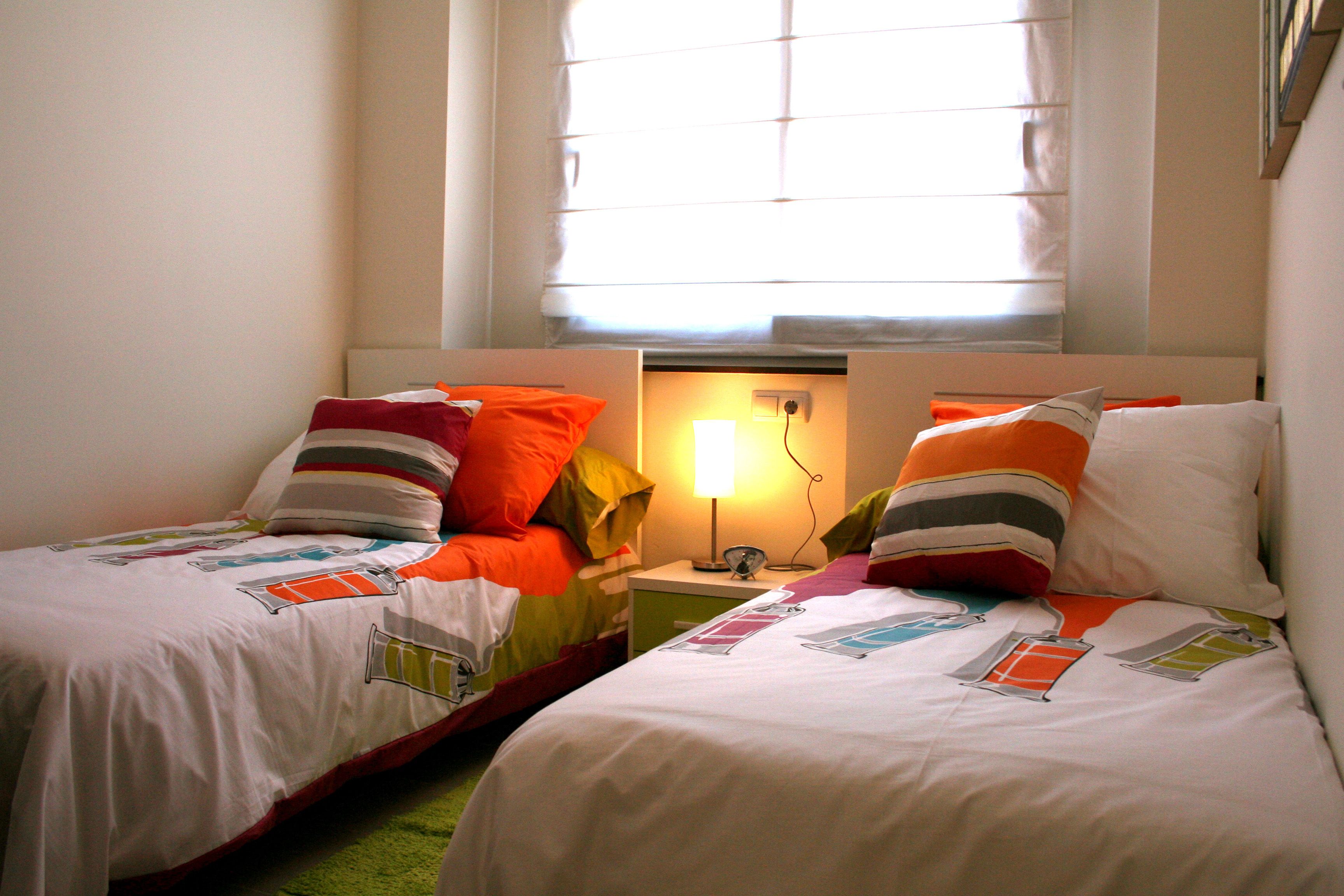 Ein Doppelzimmer mit zwei Betten, jeweils mit farbenfroher Bettwäsche und einem Nachttisch mit Lampe.