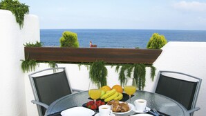 Une table dressée pour le petit-déjeuner, avec vue sur la mer, comprenant des fruits, du café et un verre de jus d’orange.