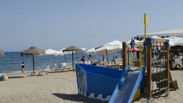 Relax by the ocean with a fun playground for kids and comfortable seating areas under shaded umbrellas.
