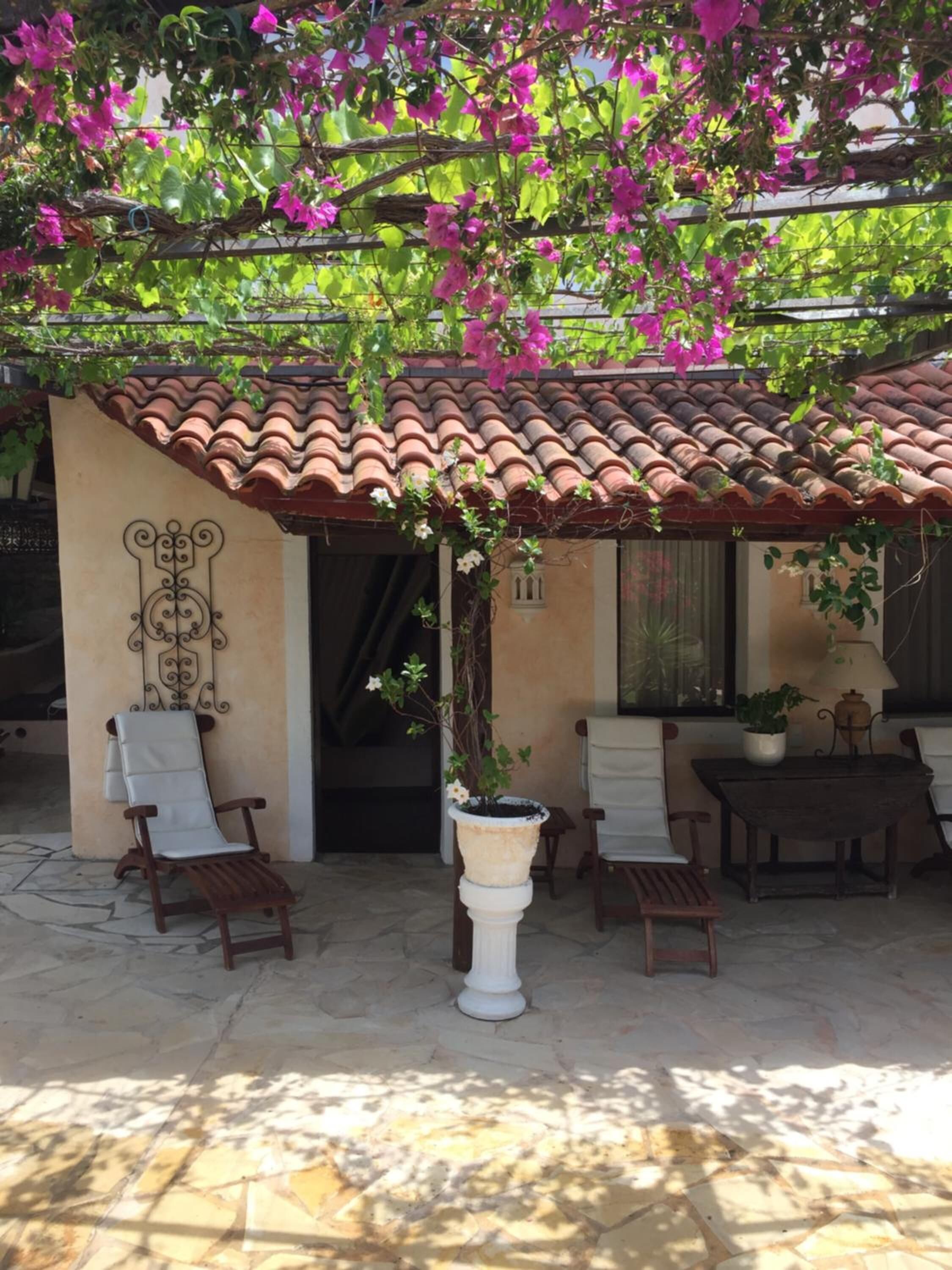 Un patio couvert avec un toit en tuiles, une colonne blanche et un pot de fleurs.