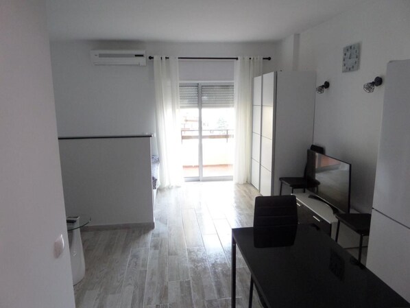 A modern, well-lit room with a dining area, a TV, and a sliding glass door leading to an outdoor balcony. - Clube DOS Arcos (Portimao)