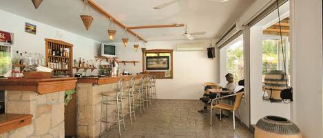 A bar area with stone counters, metal chairs, and a television.