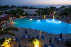 A large swimming pool with lounge chairs and umbrellas, surrounded by palm trees and buildings. - Coliseum Studios & Apartments (Rhodes)