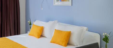 A hotel room with a bed, two pillows, a nightstand, a framed picture on the wall, and a vase with flowers.