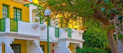 A two-story building with a yellow facade, green window frames, and a balcony with white railings.