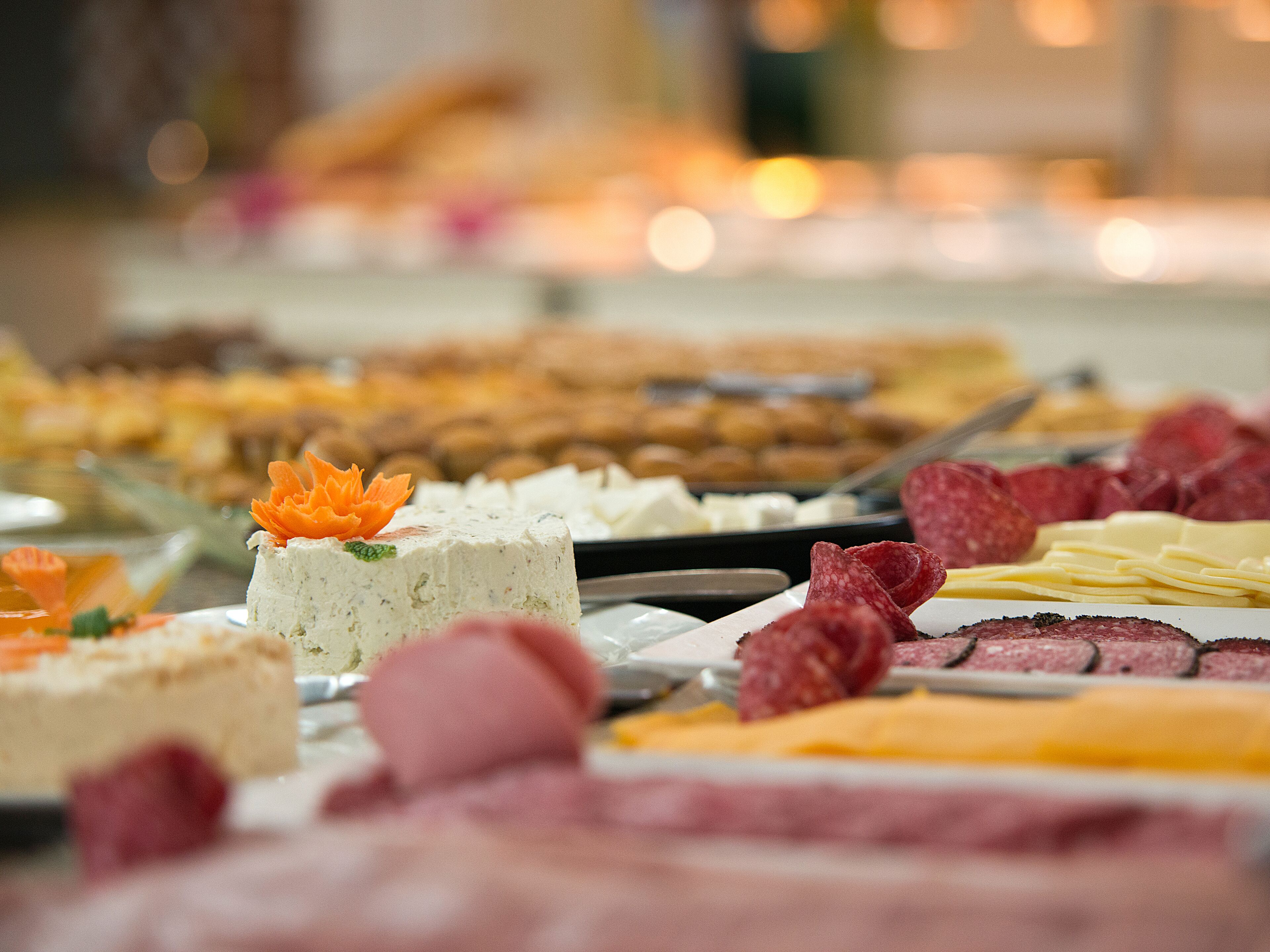 A buffet with various food items including a cake with a decorative topping, assorted meats, and cheese.