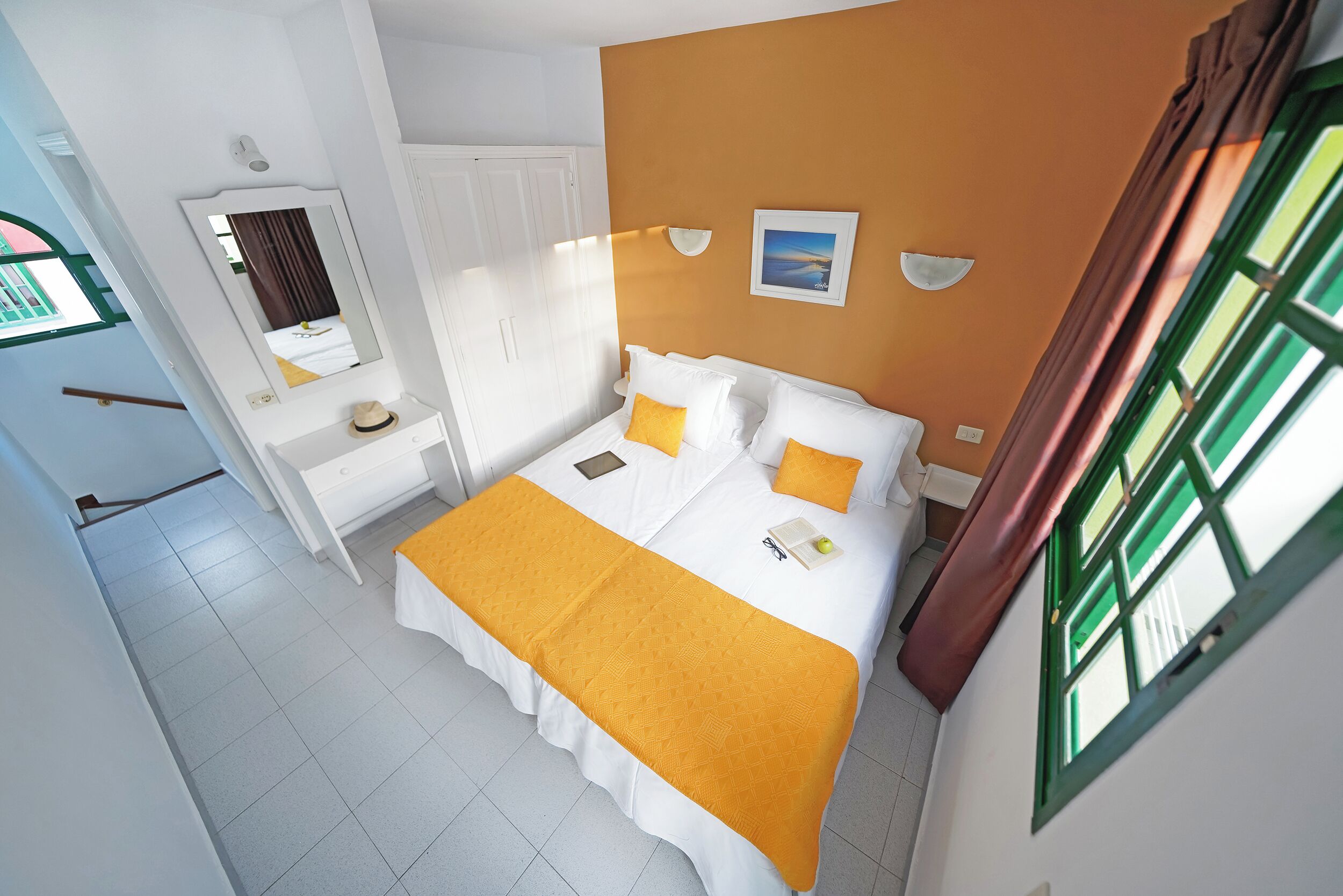 A bedroom with a bed, bedside table, mirror, and a window.