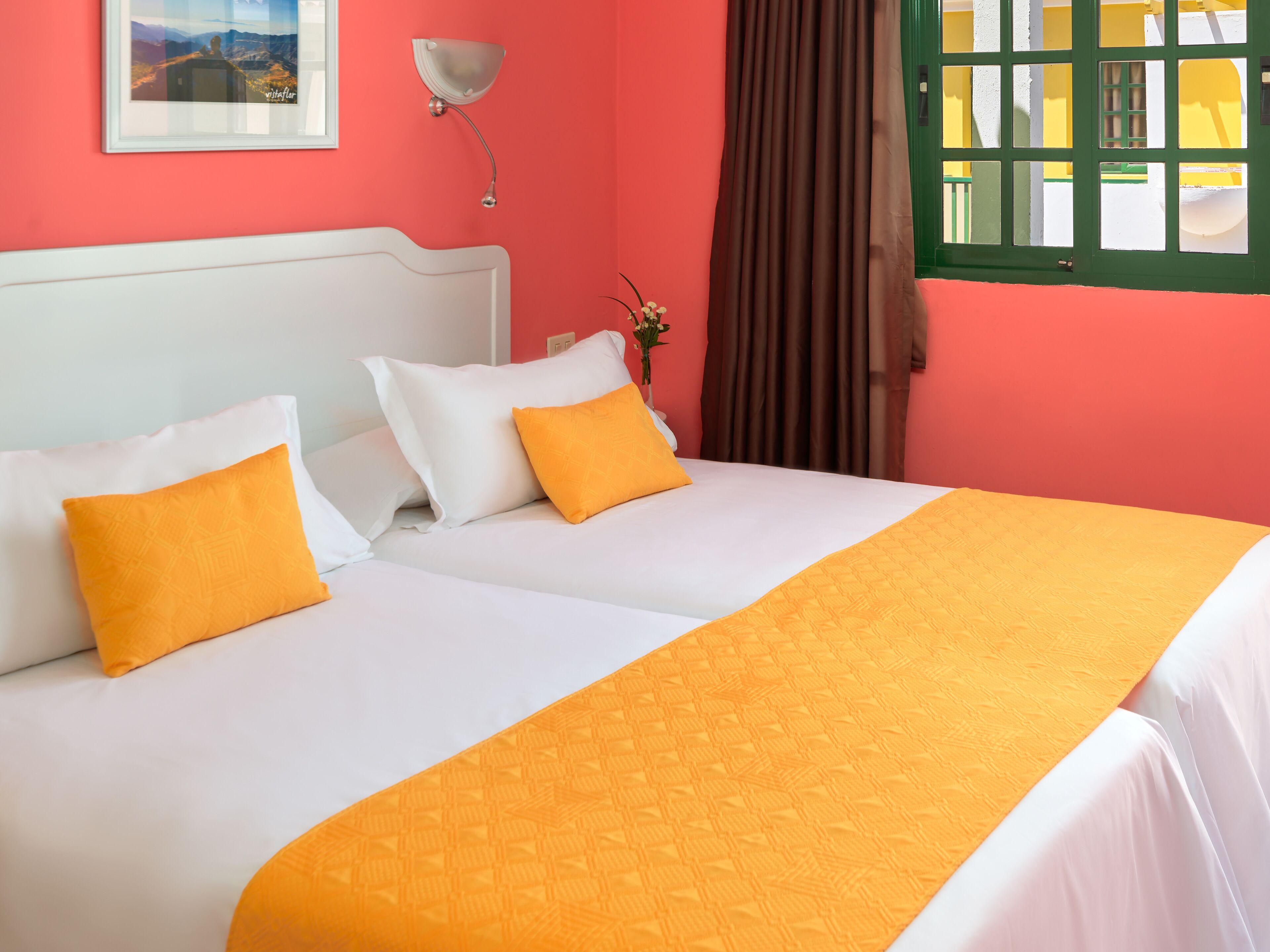 A hotel room with a white bed, orange pillows, and a large orange bedspread.
