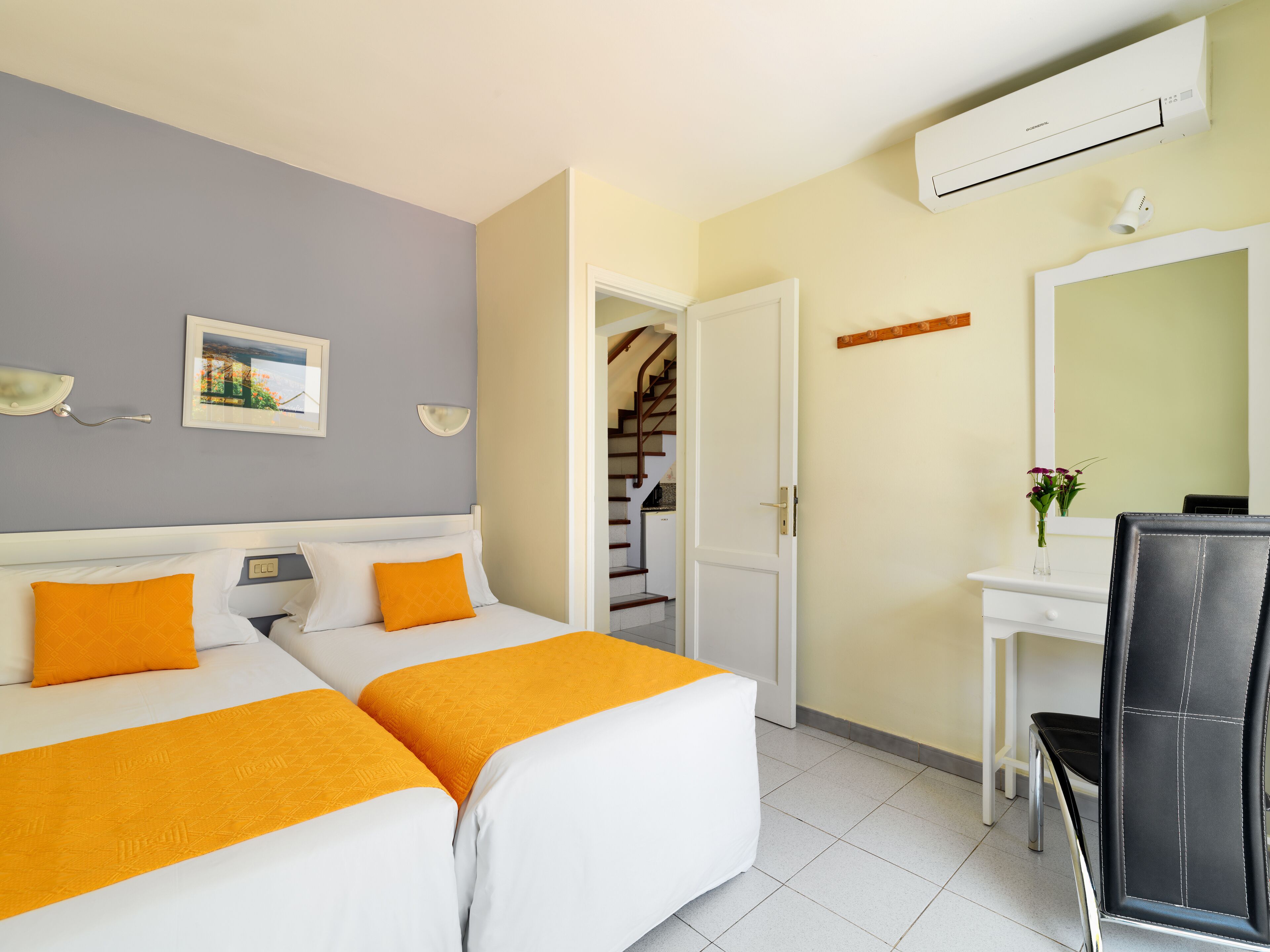 A hotel room with two beds, a desk, a chair, a mirror, and an air conditioning unit.