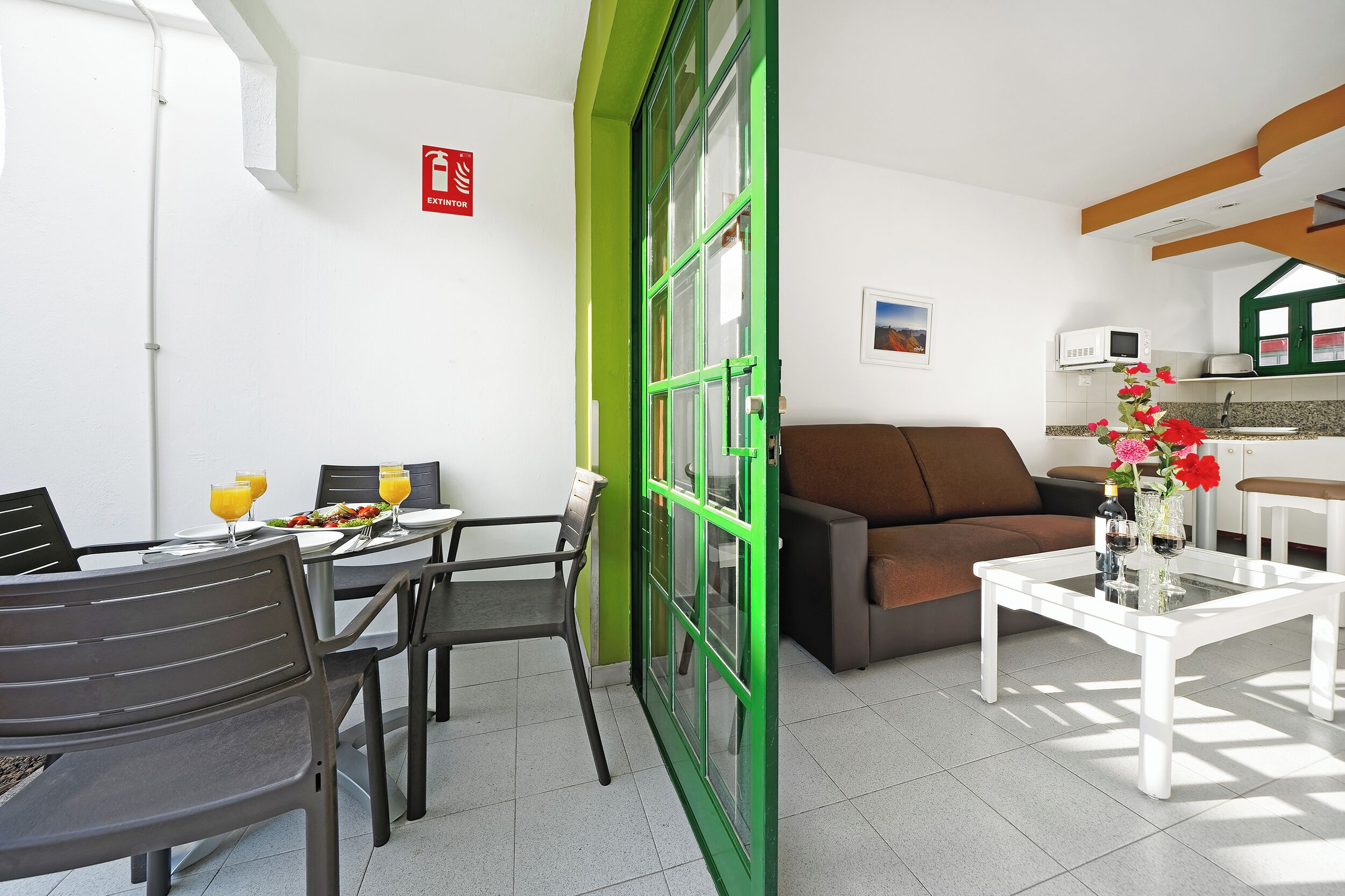 A modern room with a dining table, chairs, a sofa, a coffee table, and a kitchen area.