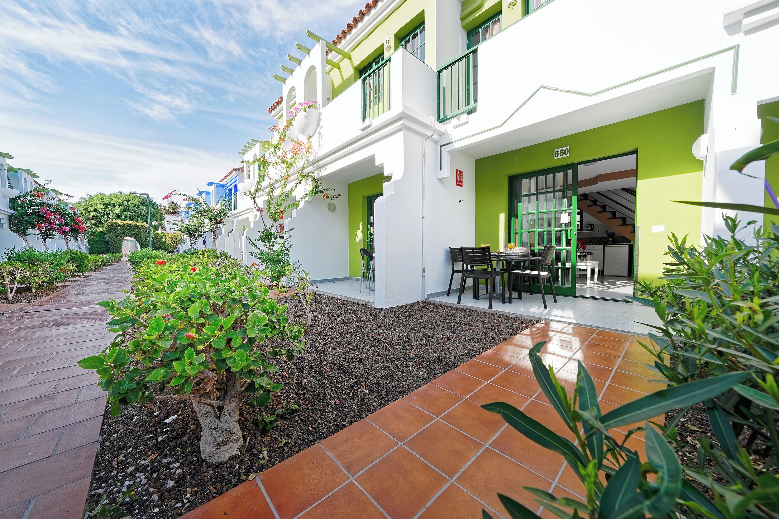 A building with a green and white facade, a paved walkway, and a small patio area with outdoor furniture.