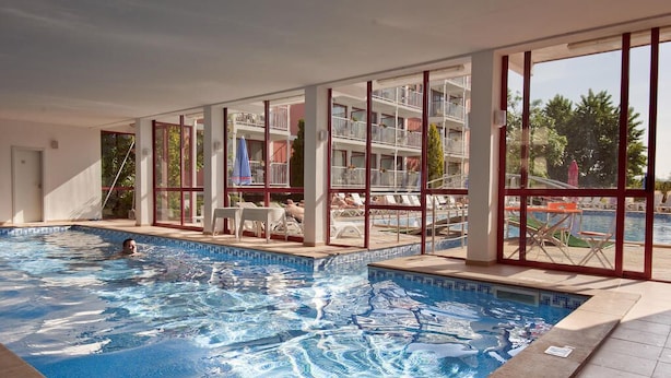 Une piscine intérieure à l’eau claire, entourée de grandes fenêtres et offrant une vue sur un immeuble doté de nombreux balcons.