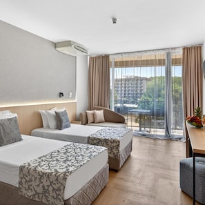 A hotel room with two beds, a sofa, a dining table, and a view of a building and trees. - Longosa (Sunny Beach)