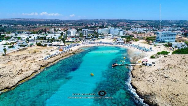 A coastal resort with a clear turquoise sea, a sandy beach, and a row of sunbeds. - Florence (Ayia Napa)