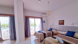 A hotel room with two beds, a dining area, and a view of an outdoor pool. - Florence (Ayia Napa)