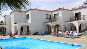 A swimming pool with lounge chairs and a slide, surrounded by white buildings with arches and balconies. - Florence (Ayia Napa)