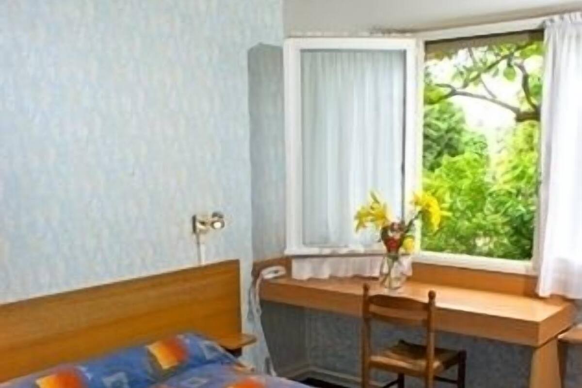 A hotel room with a bed, a desk, and a window with curtains.