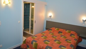 A bedroom with a bed, a walk-in closet, and a bathroom with a glass door. - Hôtel le Lyon Bron (Bron)