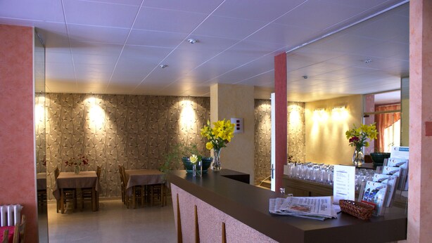A hotel reception area with a counter, seating area, and decorative wall panels. - Hôtel le Lyon Bron (Bron)