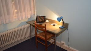 A small room with a wooden chair, a desk, a laptop, a lamp, and a radiator. - Hôtel le Lyon Bron (Bron)