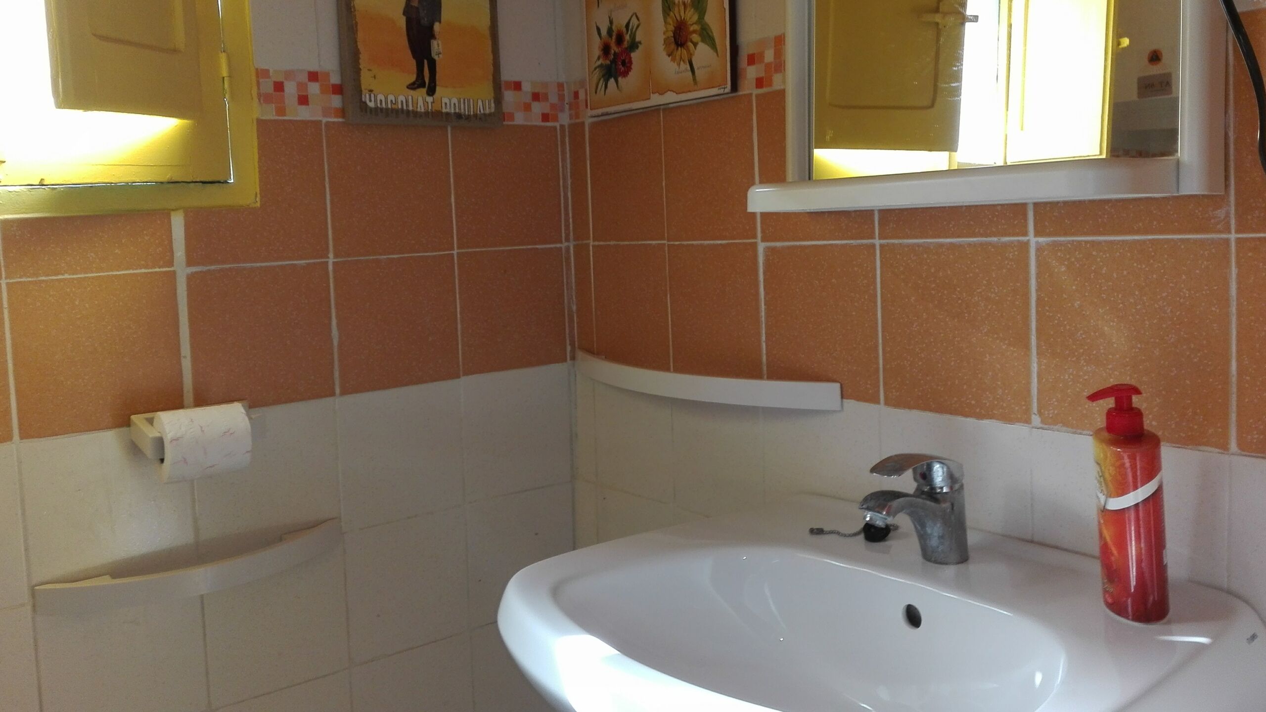 Un baño con un lavamanos blanco, un dispensador de jabón rojo y un espejo sobre el lavamanos.