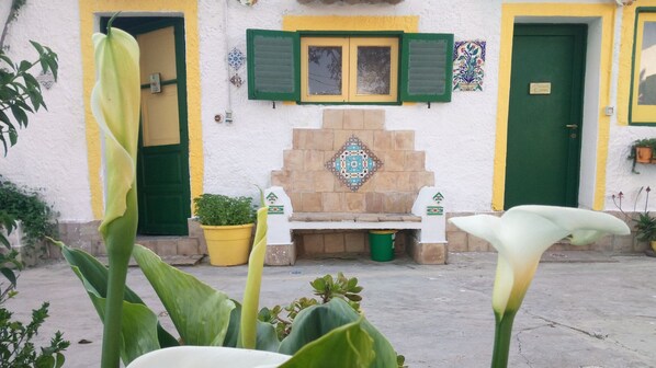 Un edificio con chimenea de piedra, contraventanas verdes y un banco en la fachada.