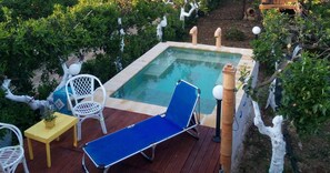 A small outdoor pool area with a blue lounge chair, a white chair, and a small table with a plant. - Zagara di Sicilia (Marsala)